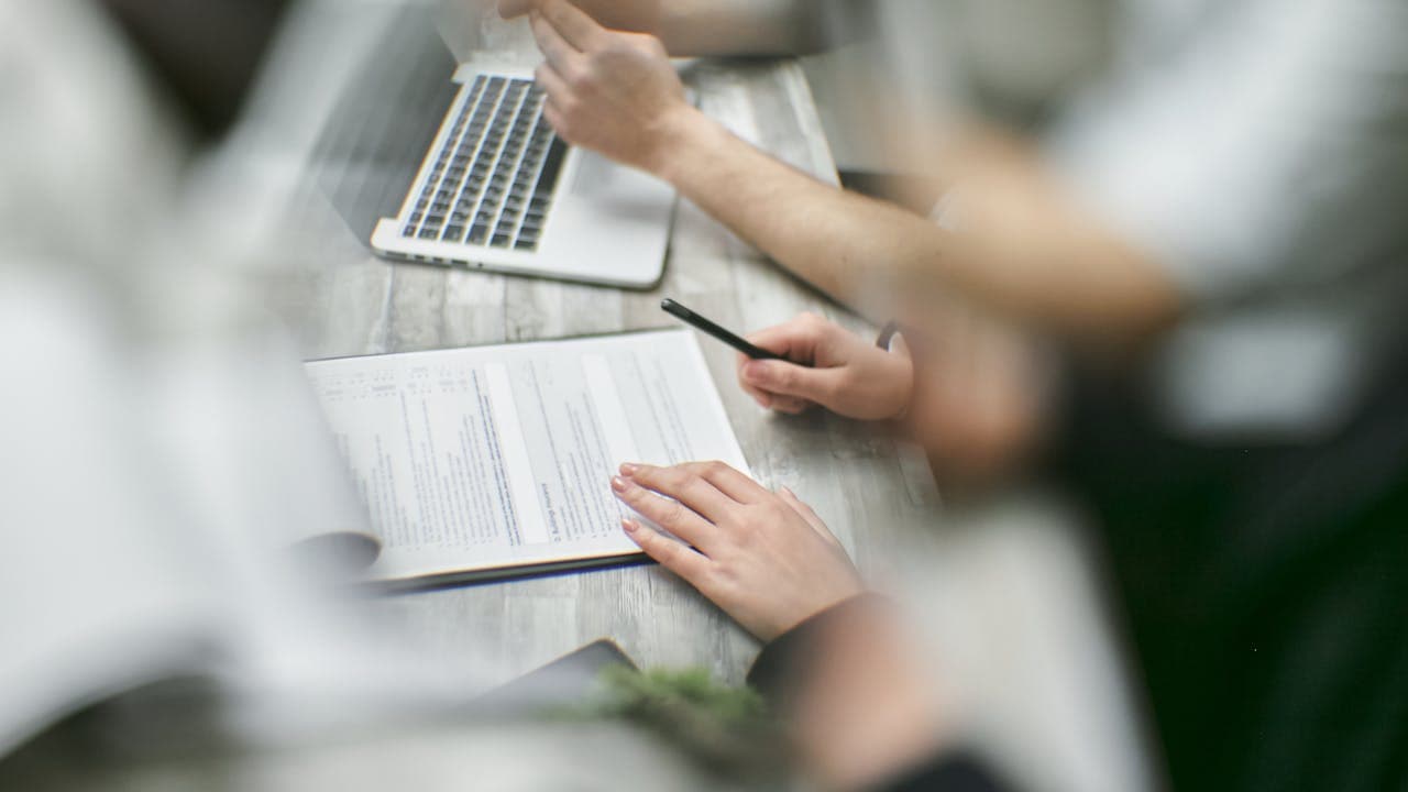 Manos sobre portátil con bolígrafo revisando datos en mesa de despacho